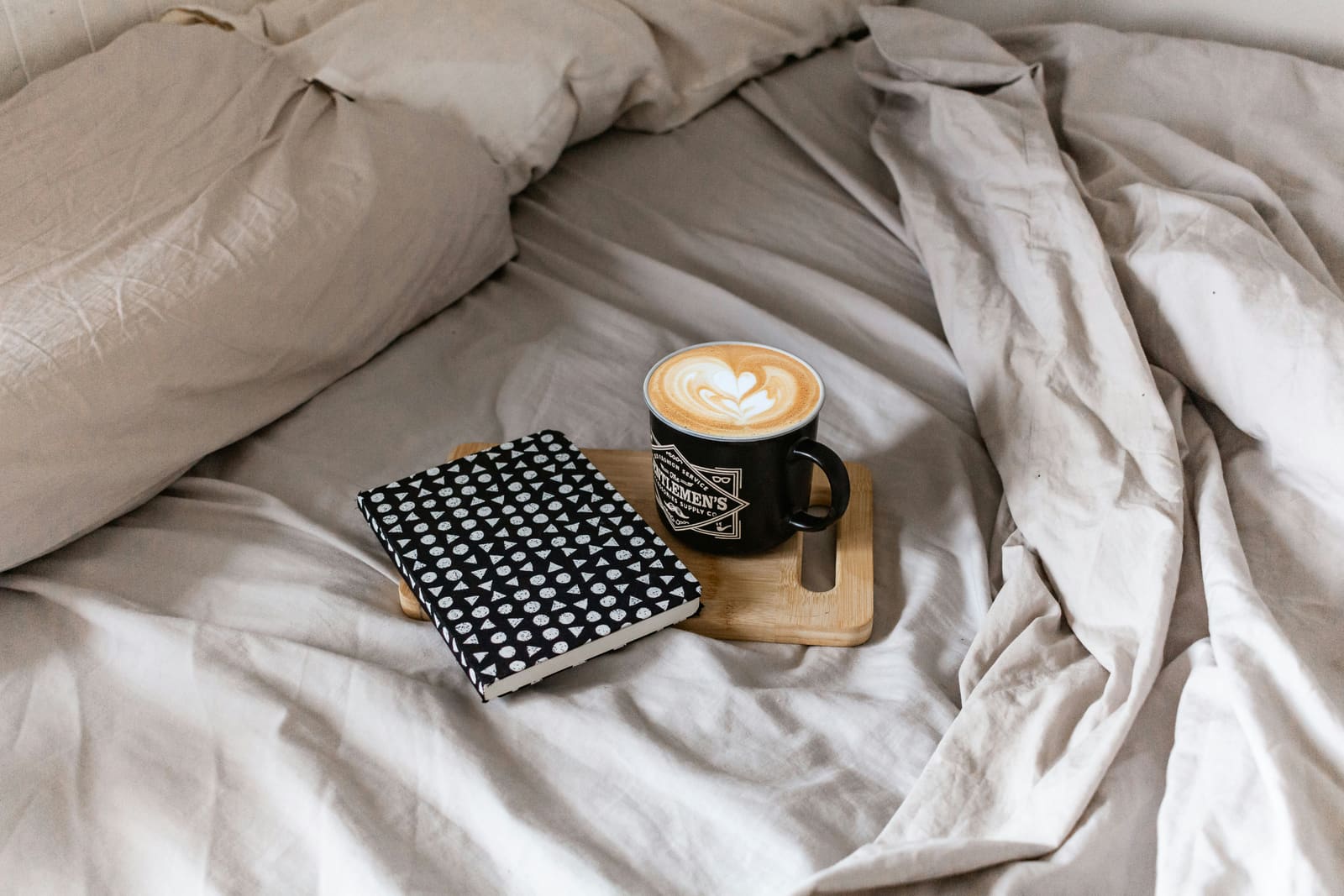 Ungemachtes Bett mit Notizbuch und Kaffeetasse